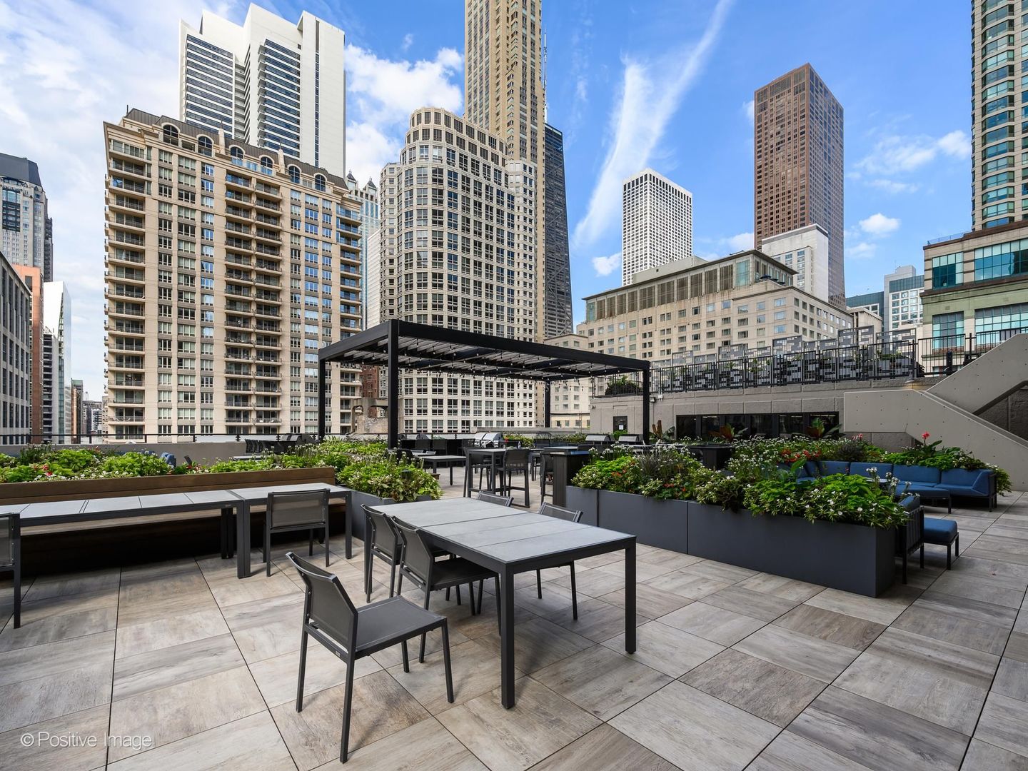 Rooftop terrace with dining furniture, planted beds, lounge seating, and a pergola among downtown high-rises.