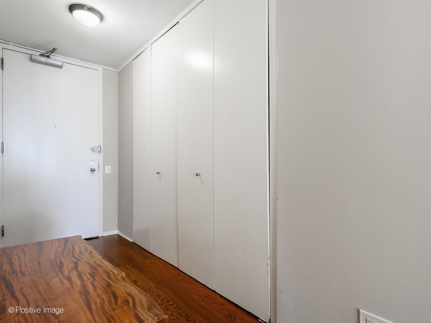 Unit entry with built-in closets, a white front door, and dark wood flooring.