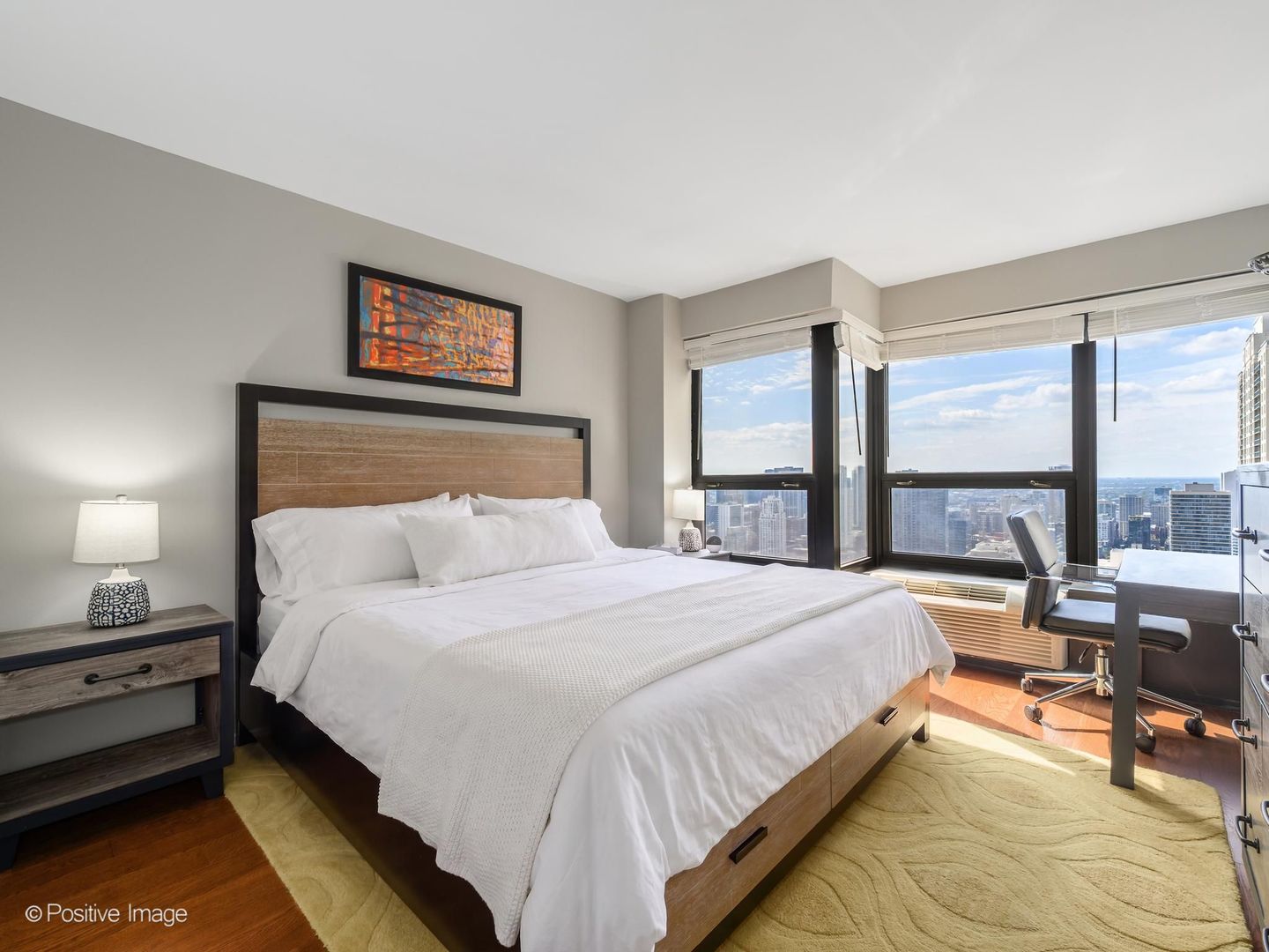 Bedroom with a large white bed and floor-to-ceiling windows overlooking the city skyline.