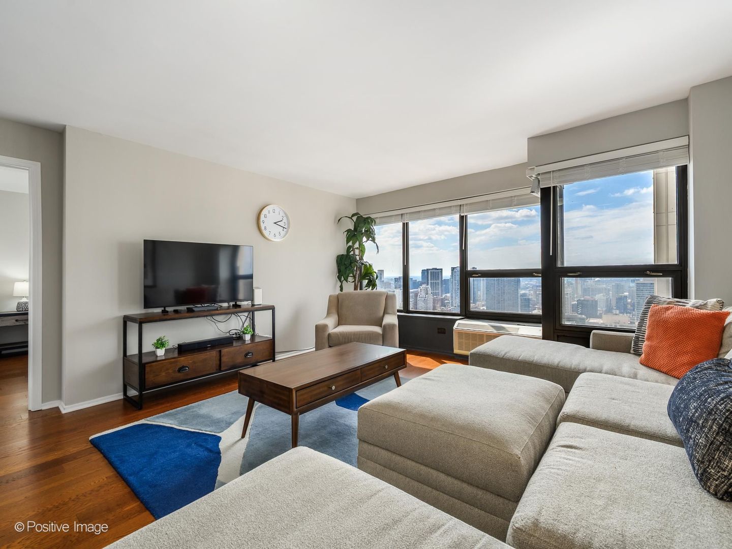 Condo living room with a sectional sofa and city skyline views through large windows.