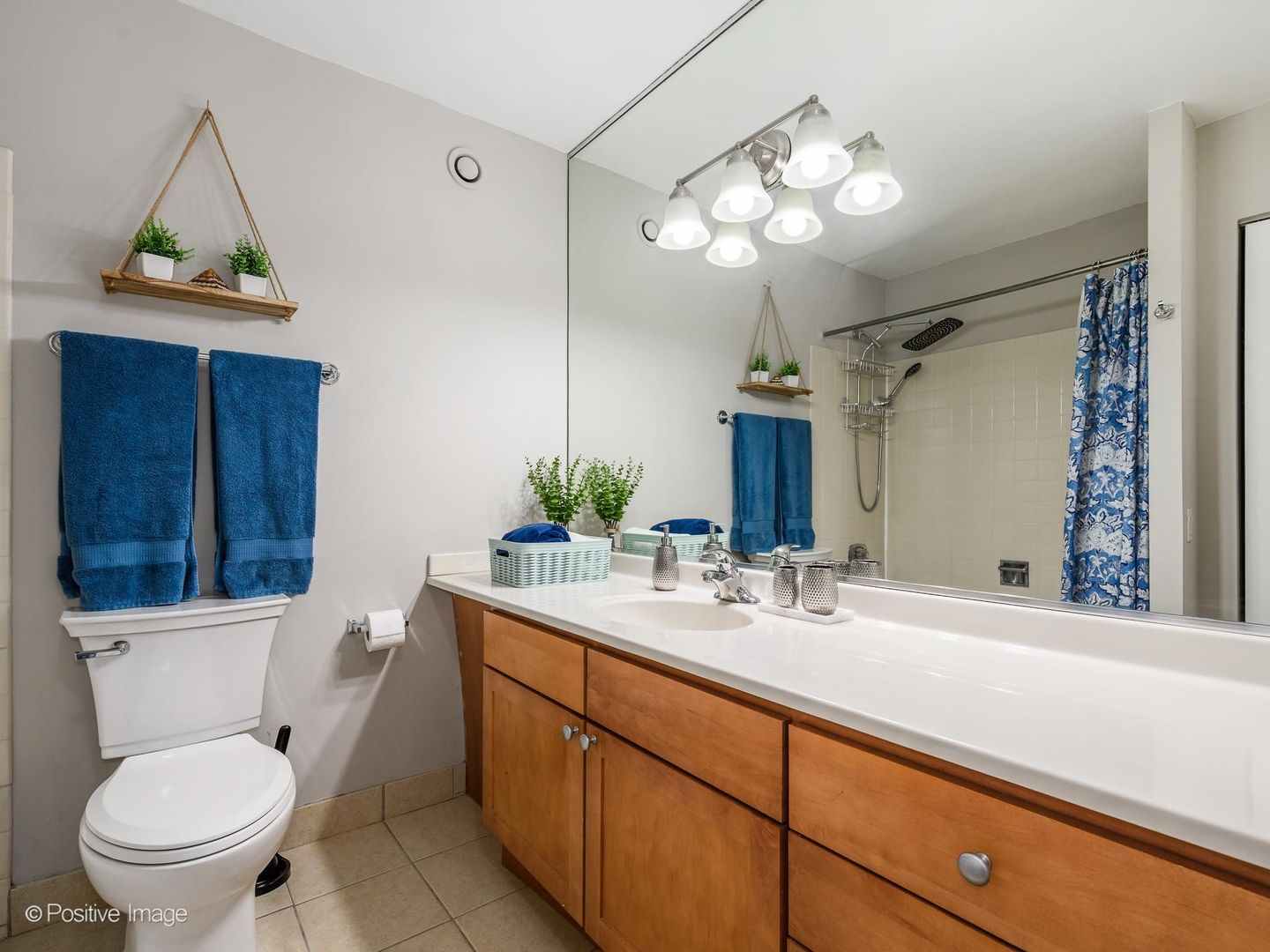 Bathroom with a wood vanity, large mirror, and tiled shower with a blue patterned curtain.