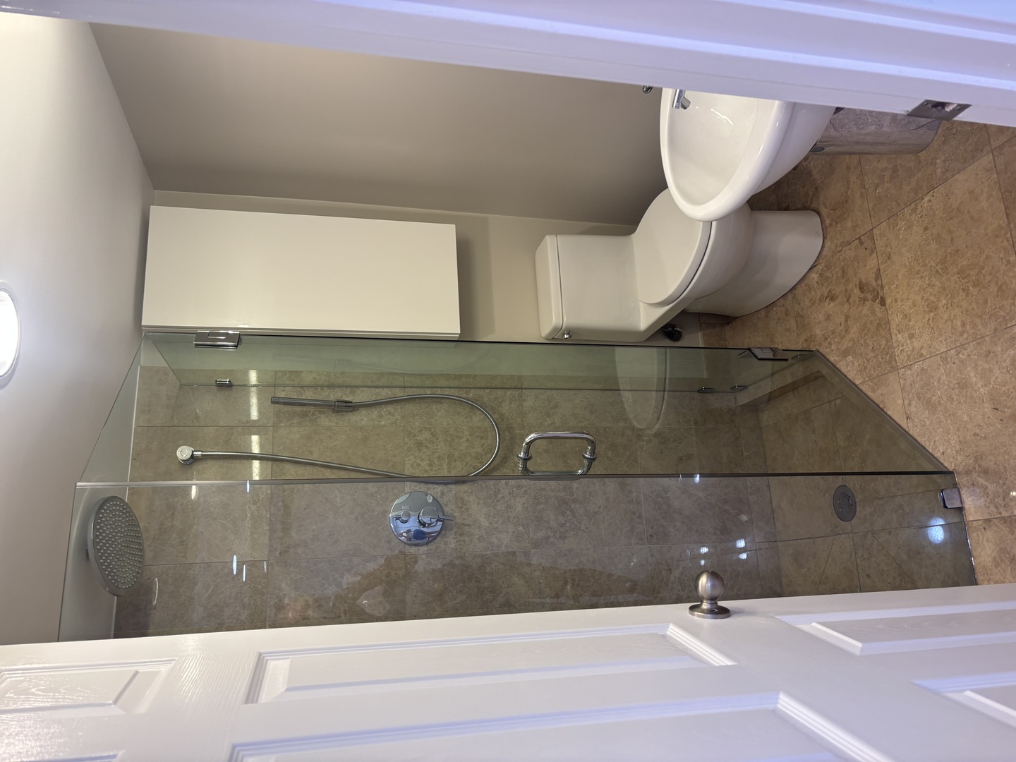 Bathroom with a glass-enclosed tiled shower, toilet, and compact wall cabinet.
