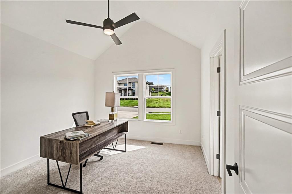 Furnished home office with a dark wood desk, vaulted ceiling, and window overlooking neighboring homes.