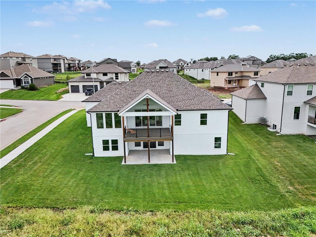 Rear aerial view of a white two-story house with a covered balcony and broad green lawn.