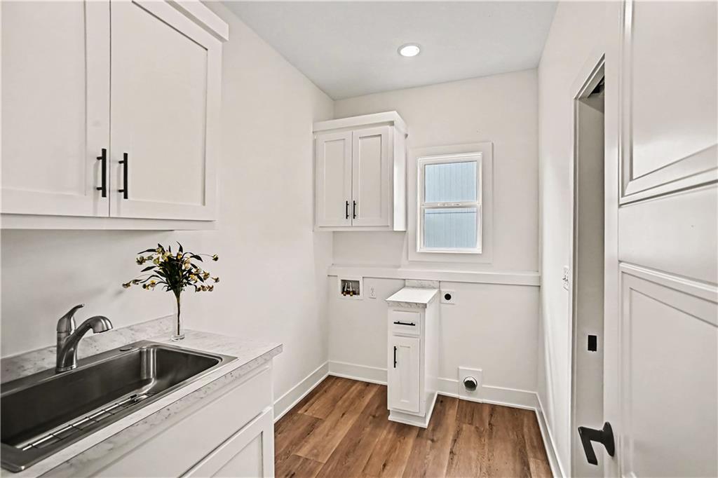 Laundry room with white cabinets, a stainless steel sink, and wood-look flooring.