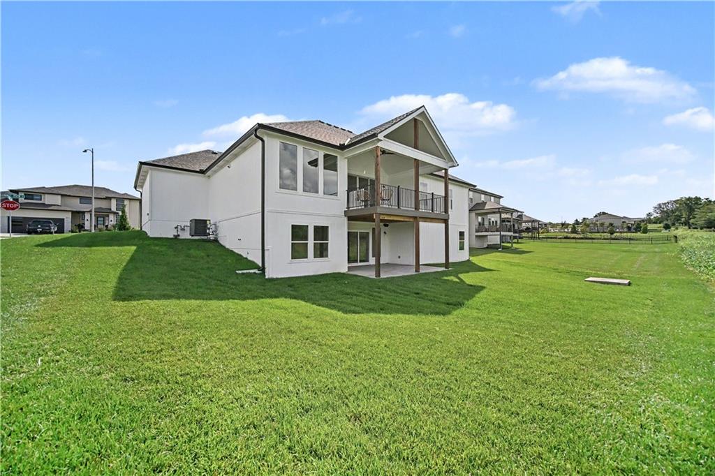 Rear of a two-story house with a covered patio, upper balcony, and broad green lawn.