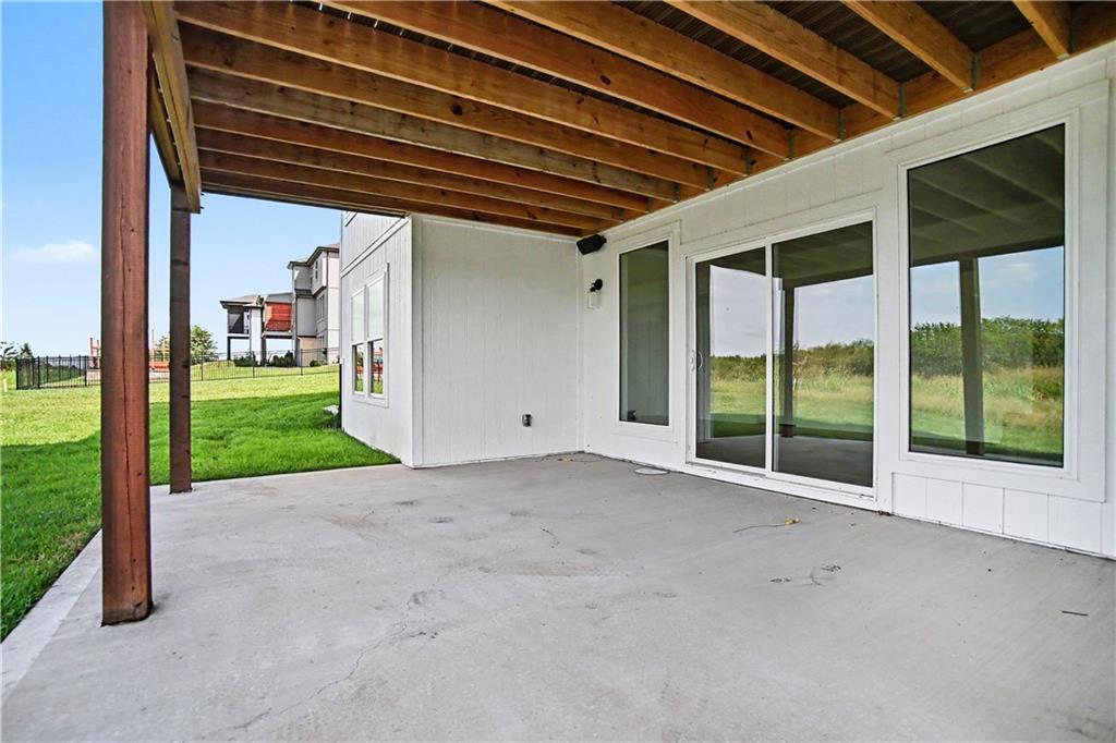 Covered concrete patio with exposed timber beams, sliding glass doors, and a lawn view.