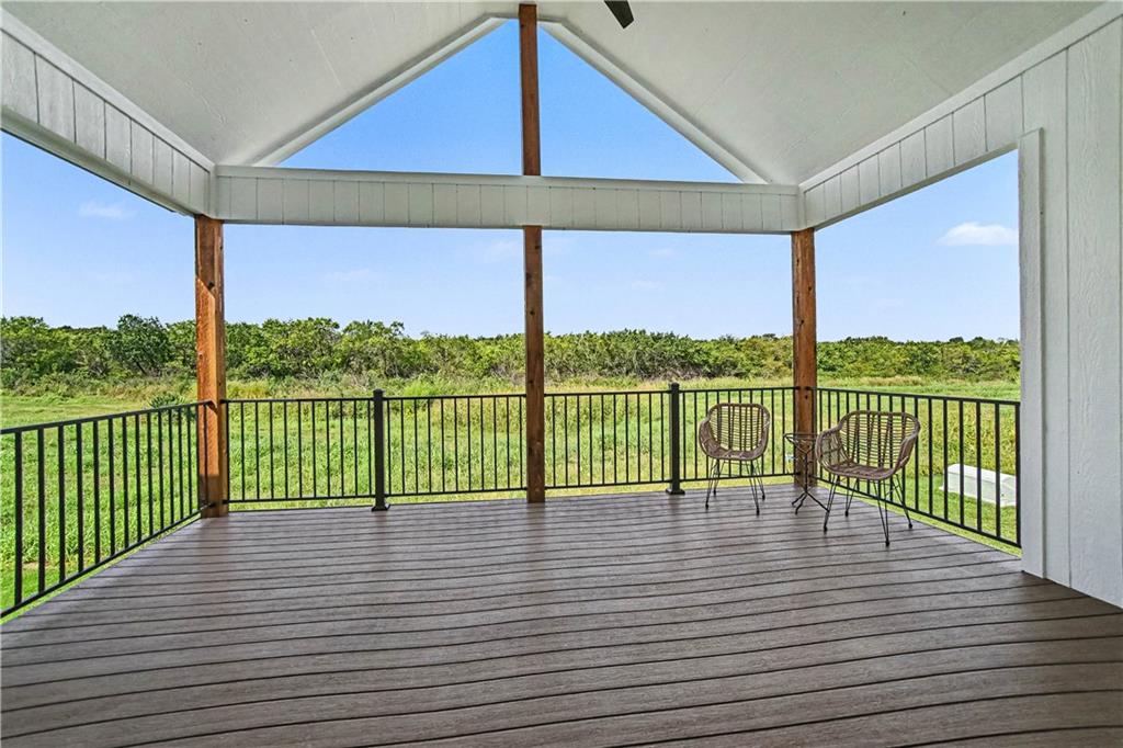 Covered deck overlooking a grassy field, with two chairs beside the black railing.