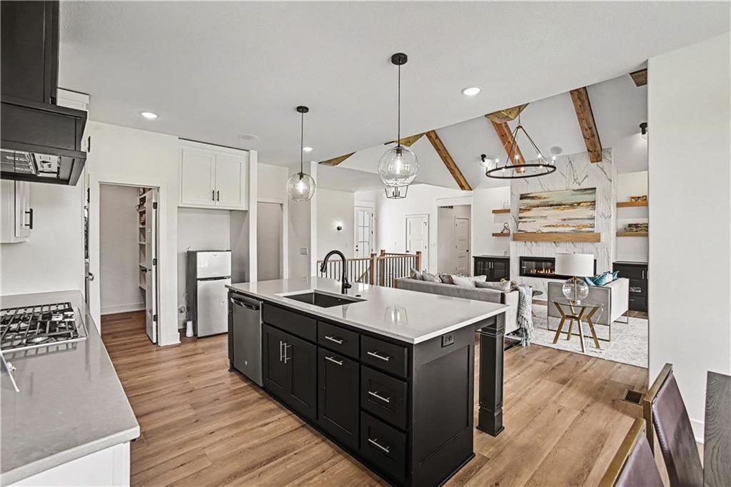 Open-plan kitchen with a large dark island, white counters, wood floors, and exposed ceiling beams.