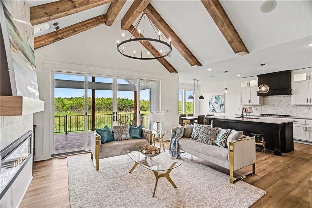 Furnished living room with vaulted wood-beam ceiling, fireplace, and sliding doors to a deck.