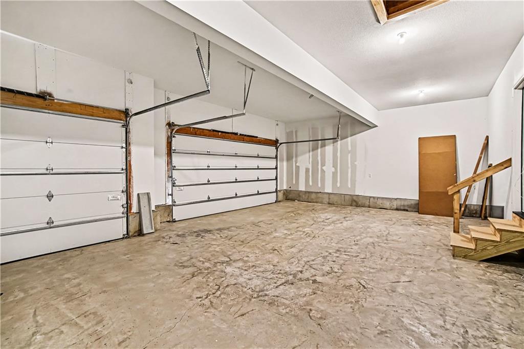 Unfinished garage with two overhead doors, a cracked concrete floor, and a rough wooden staircase.