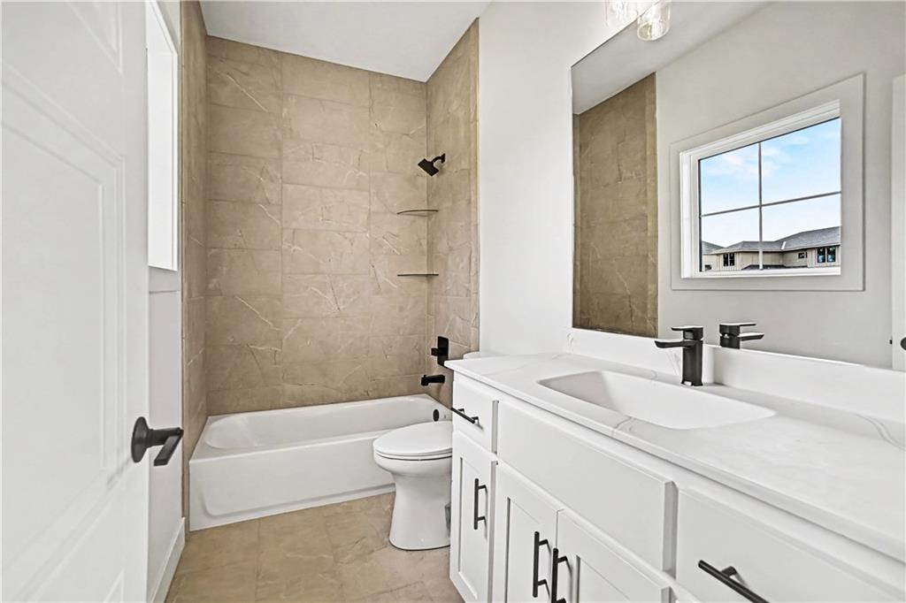 Bathroom with a white vanity, toilet, and bathtub surrounded by beige tile.