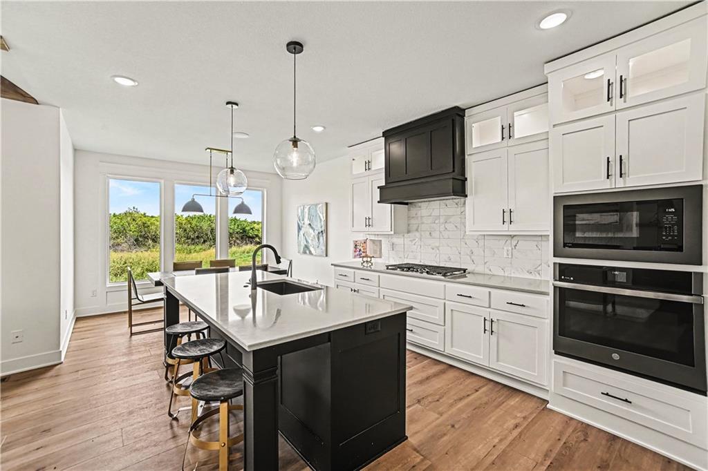 Modern kitchen with a black island, white cabinets, and large windows overlooking greenery.