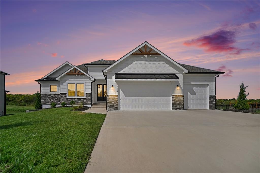 Gray single-story home with stone accents and two garage doors beneath a pink-purple dusk sky.