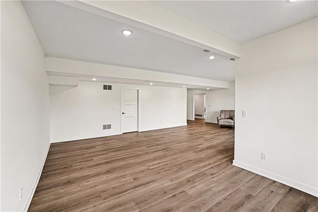Spacious room with wood-look flooring, recessed lights, and a chair near the back doorway.