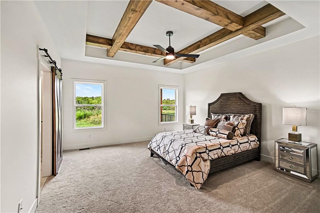 Bedroom with a patterned bed beneath exposed wooden ceiling beams and a ceiling fan.