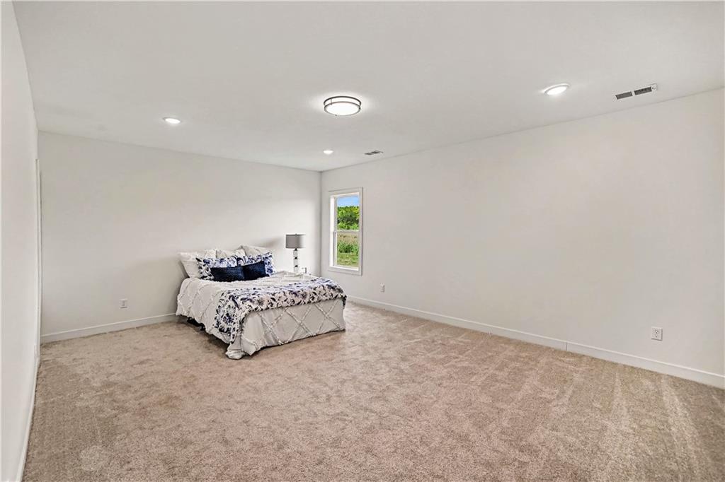 Spacious carpeted bedroom with a bed dressed in patterned white-and-blue bedding beside a window.