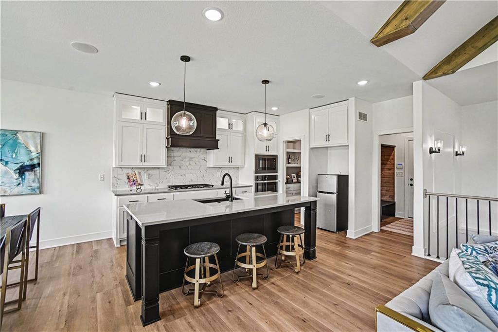 Kitchen with a large black island, white cabinets, marble-pattern backsplash, and exposed wood ceiling beams.