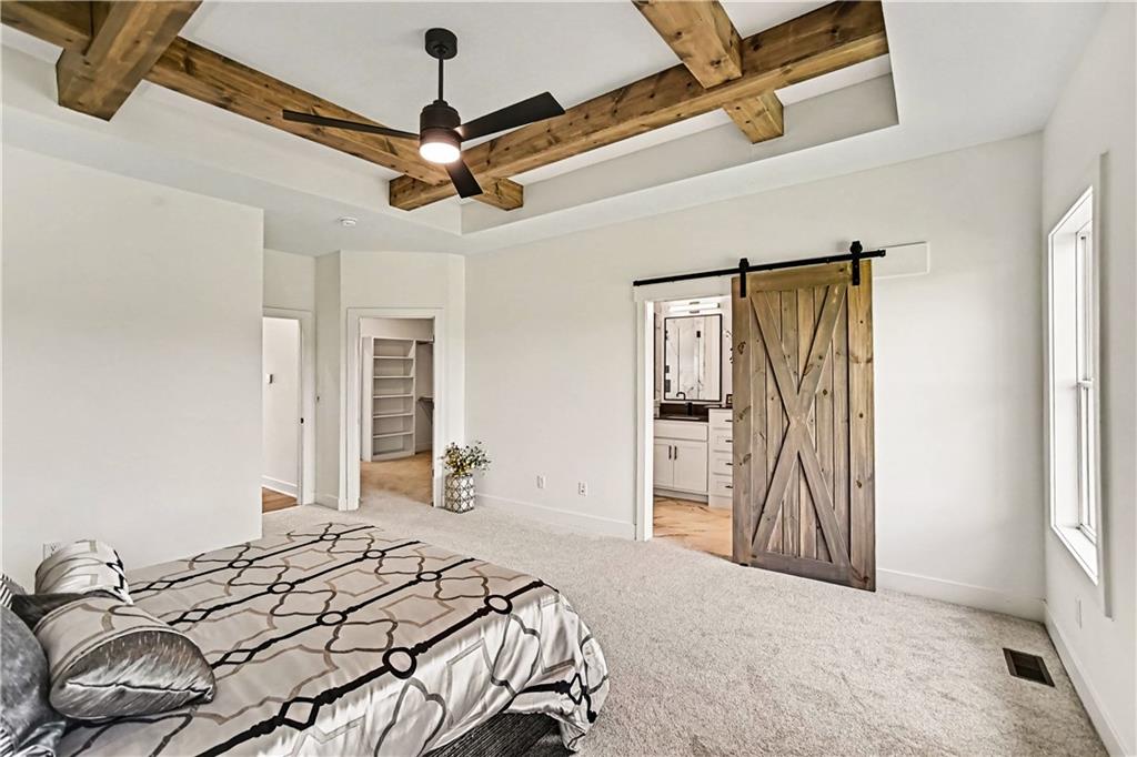 Bedroom with exposed wooden ceiling beams, a patterned bed, and a sliding barn door.