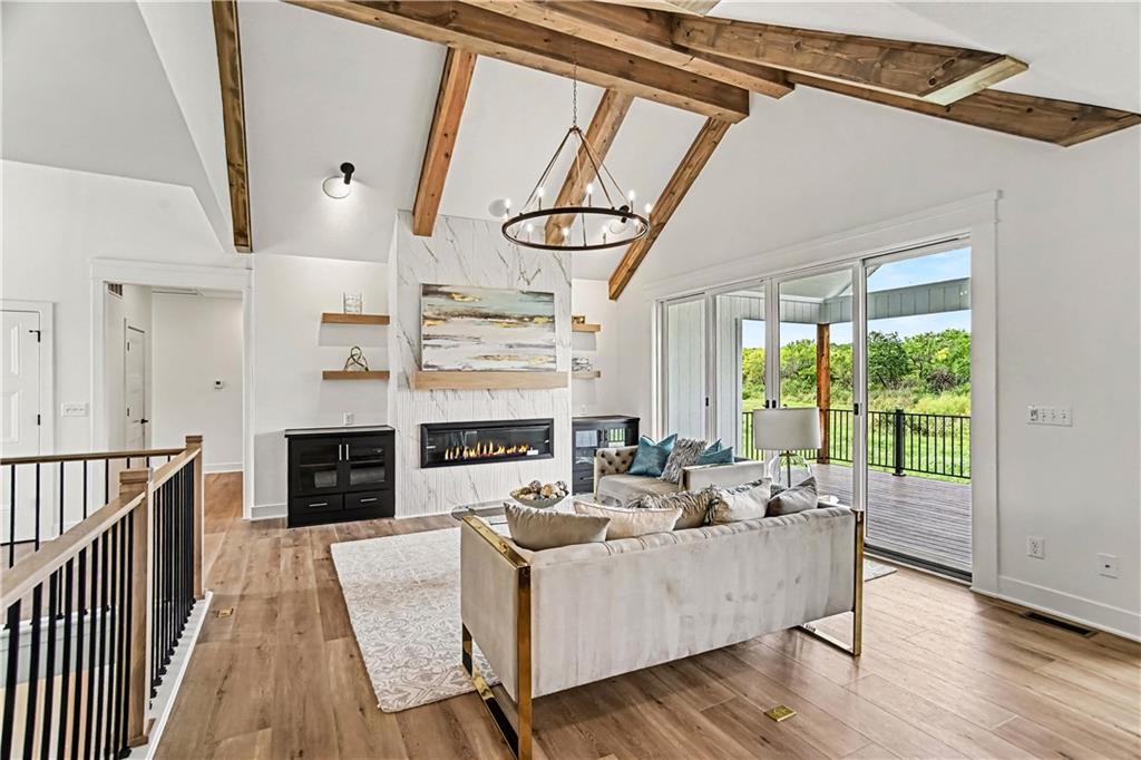 Living room with exposed wood beams, a marble fireplace, and sliding doors to a green view.