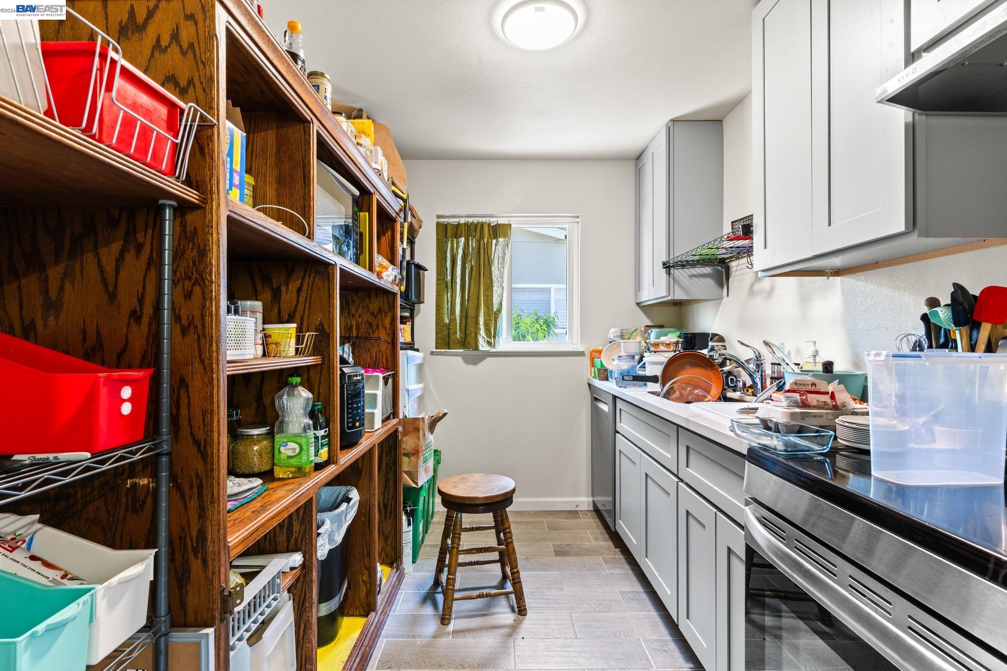 Narrow kitchen with white cabinets, crowded counters, and floor-to-ceiling wooden pantry shelves.