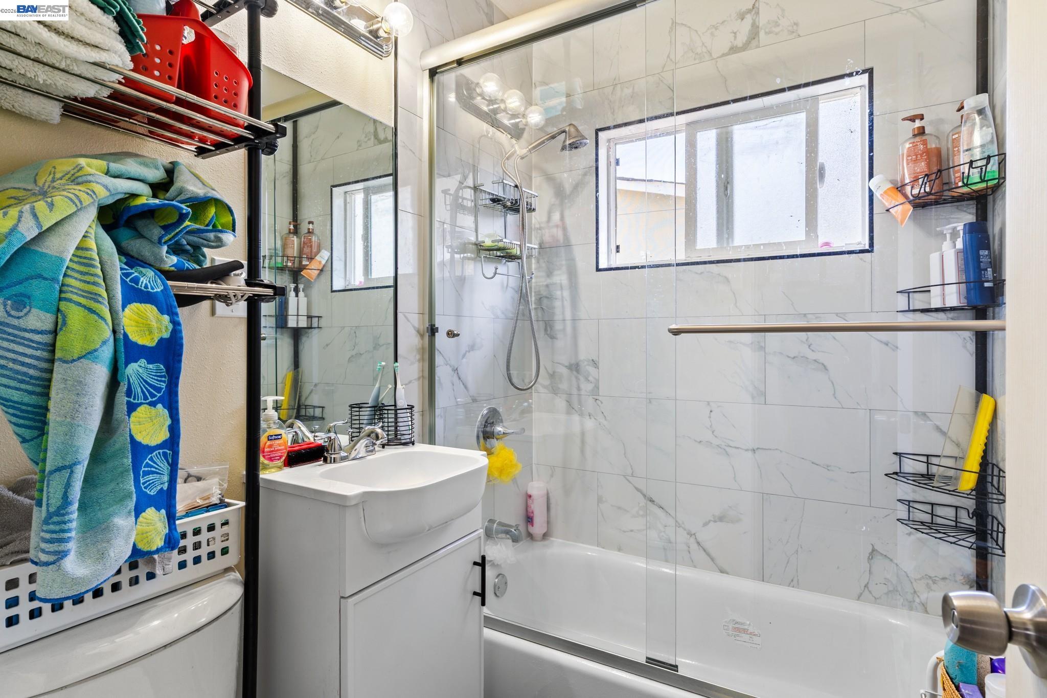 Bathroom with a glass-enclosed tub, marble-look tile, window, and white vanity.
