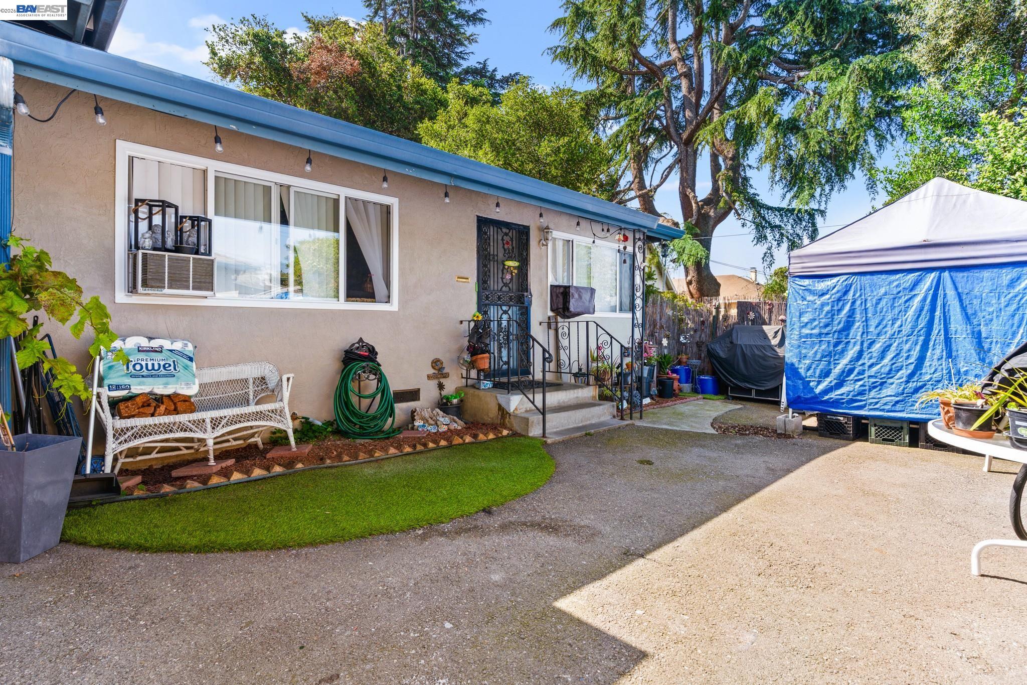 Single-story home beside a paved backyard with a small lawn and large blue-and-white canopy.