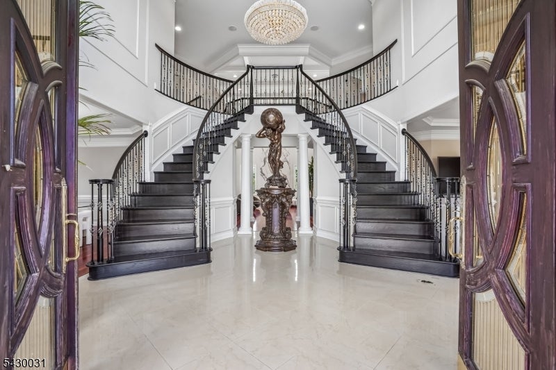 Grand foyer with twin curved staircases, a central bronze sculpture and fountain, and a crystal chandelier.