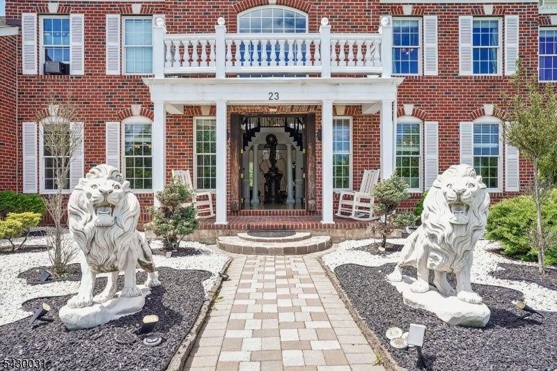 Red-brick home entrance with a white balcony, paved walkway, and matching lion statues.