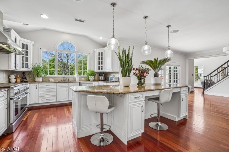 Bright kitchen with a large granite island, white cabinetry, pendant lights, and hardwood floors.