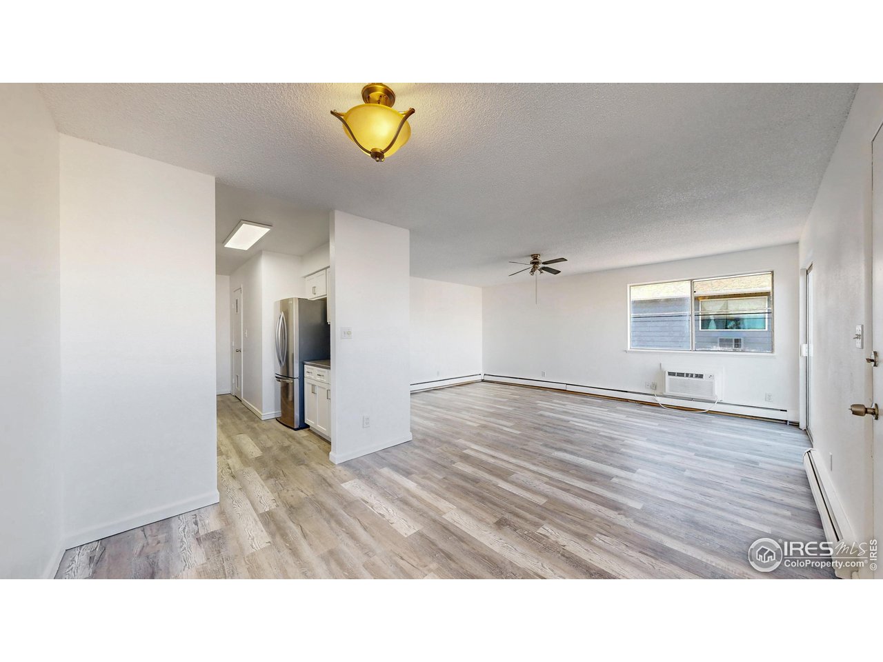 Open living room with gray wood-look floors, ceiling fan, and compact kitchen.