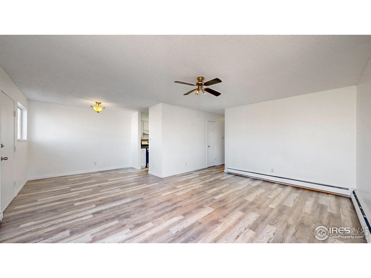 Unfurnished living room with wood-look flooring, a ceiling fan, and baseboard heating.