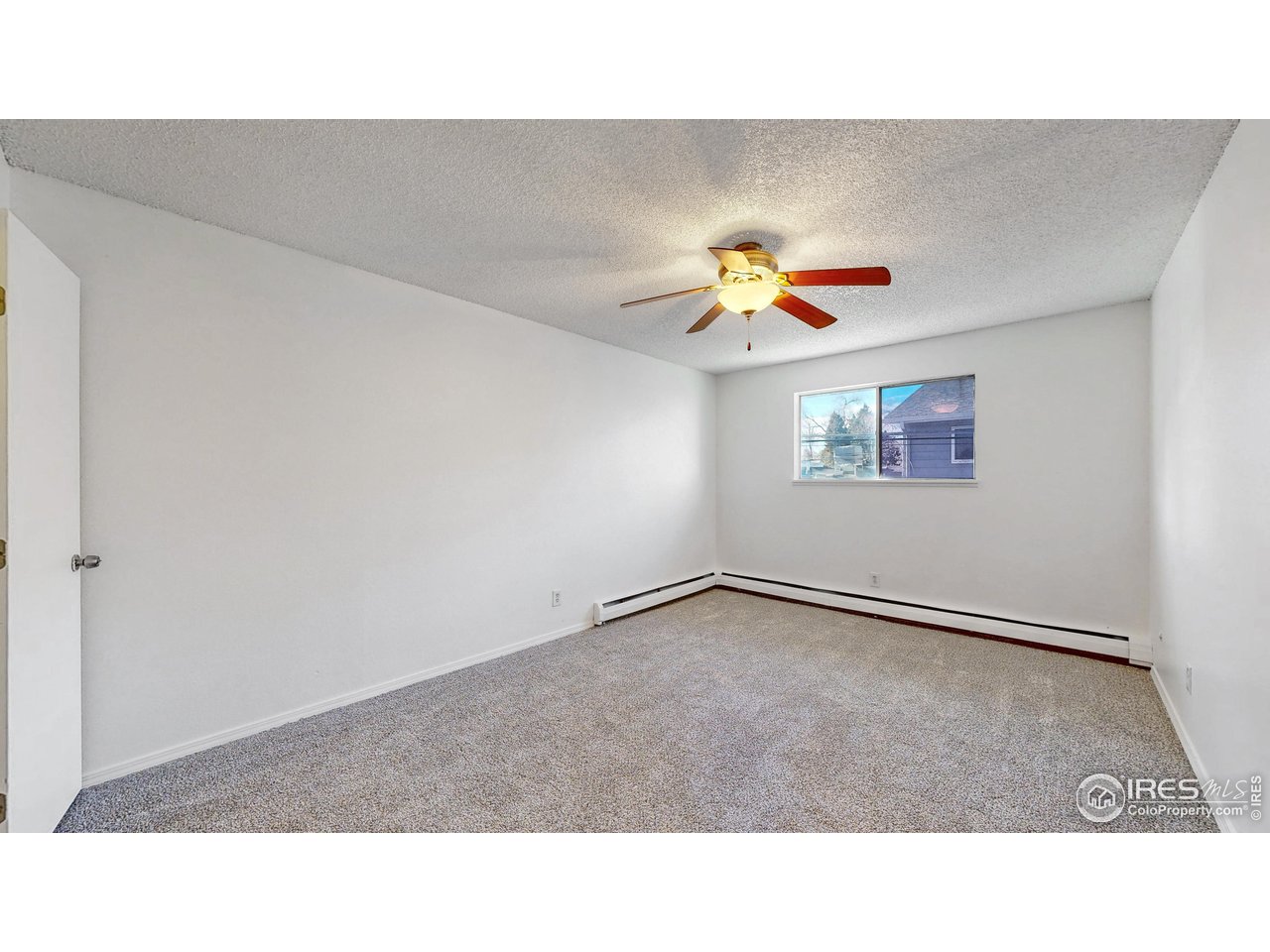 Empty bedroom with gray carpet, a ceiling fan, and a window above the baseboard heater.