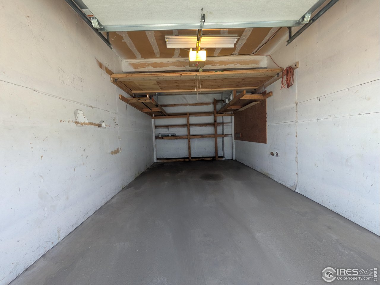 Empty garage with a concrete floor and elevated wooden storage shelves at the back.