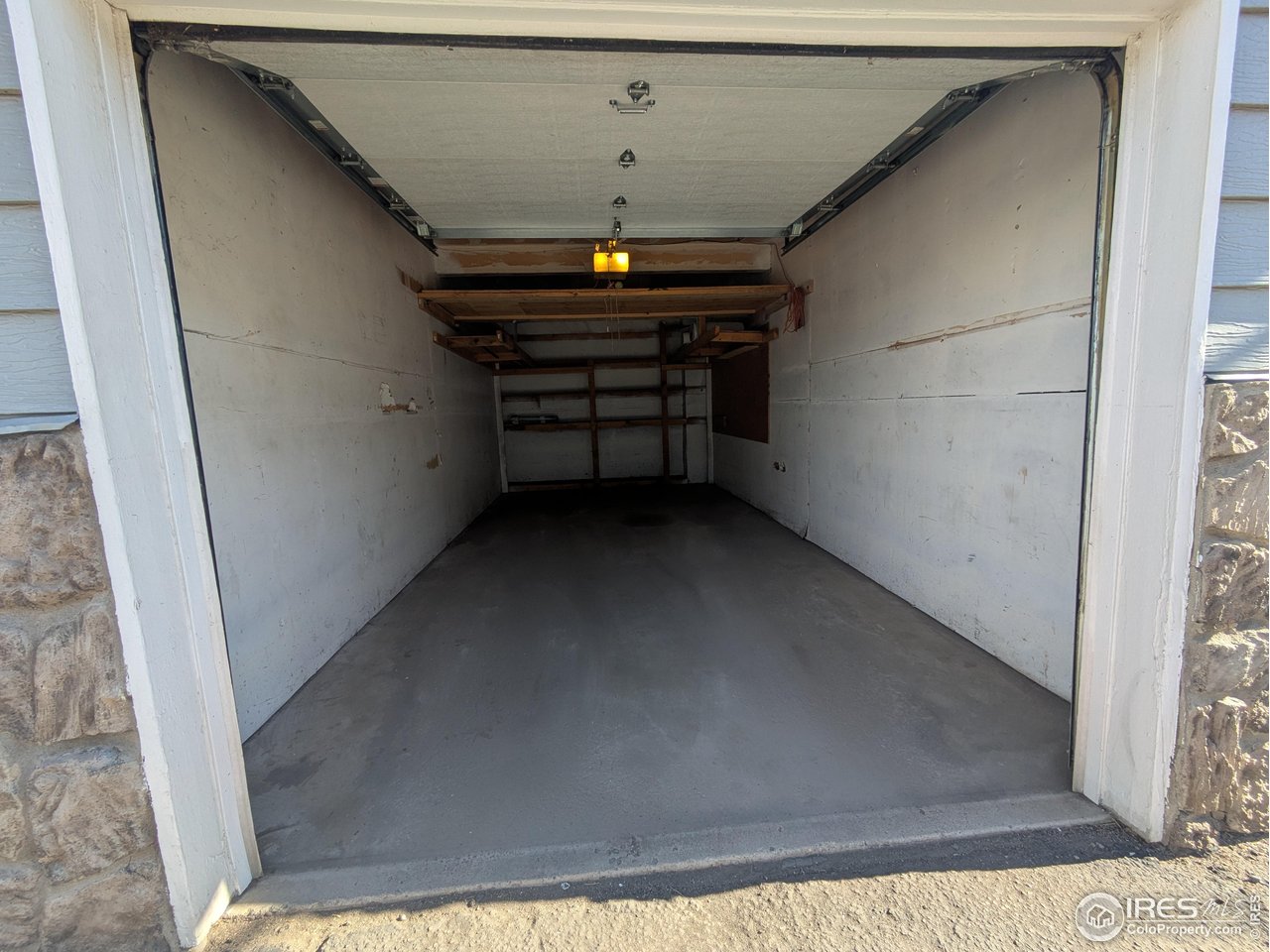 Empty garage with a raised overhead door, concrete floor, and wooden shelves at the back.
