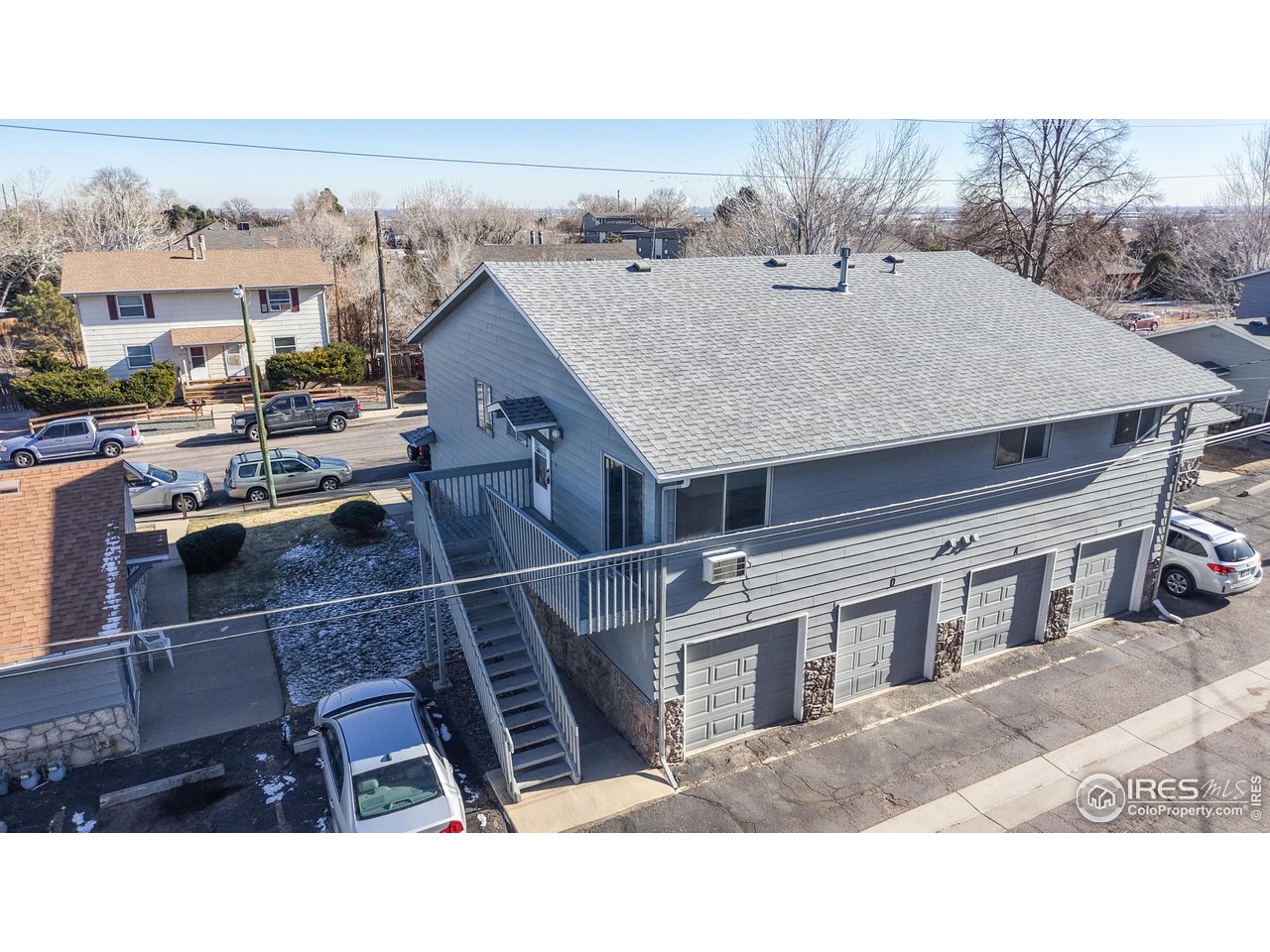 Aerial view of a gray multi-unit building with exterior stairs and street-facing garage doors.