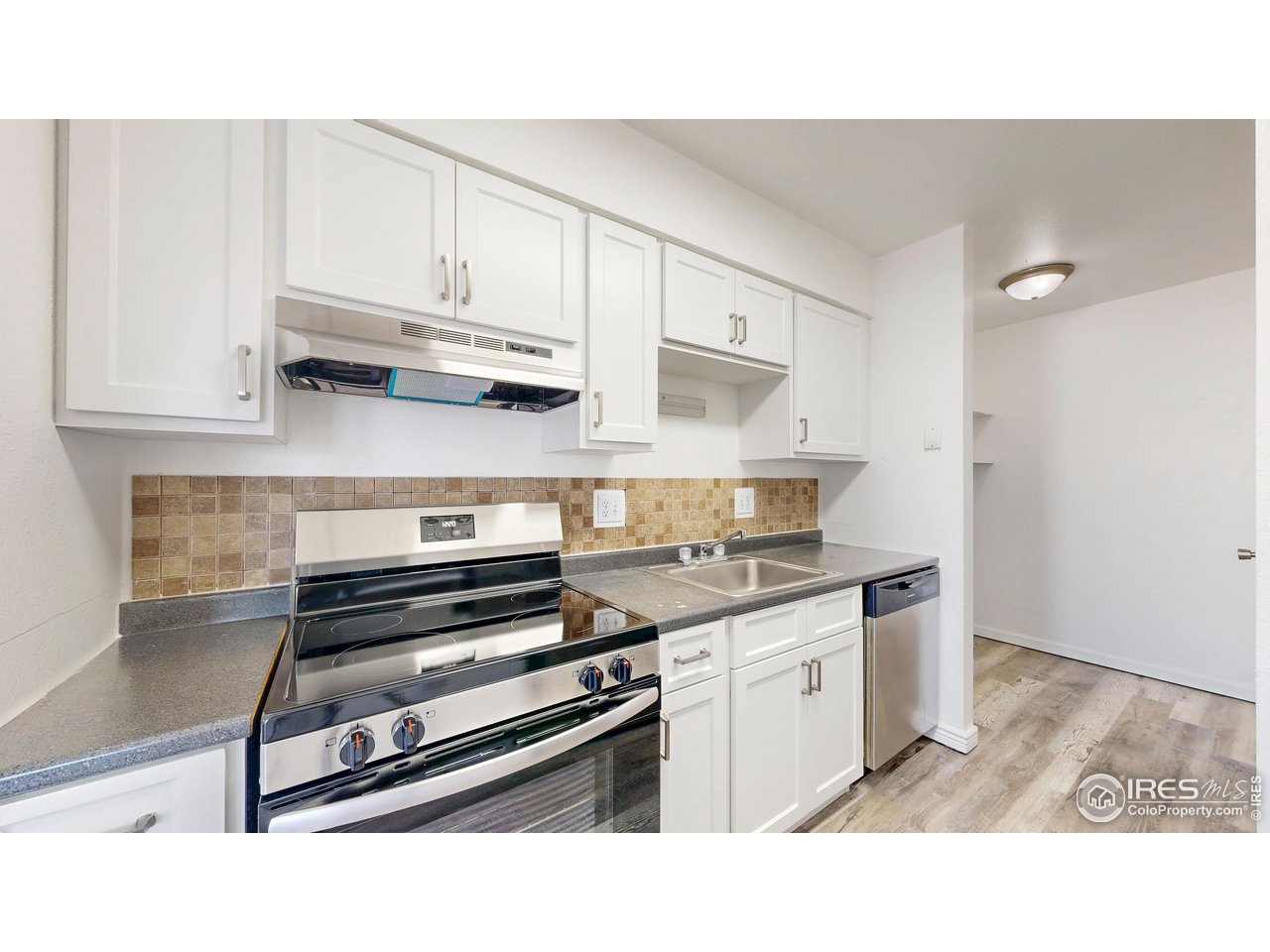 Kitchen with white cabinets, stainless steel appliances, gray counters, and a tan tile backsplash.