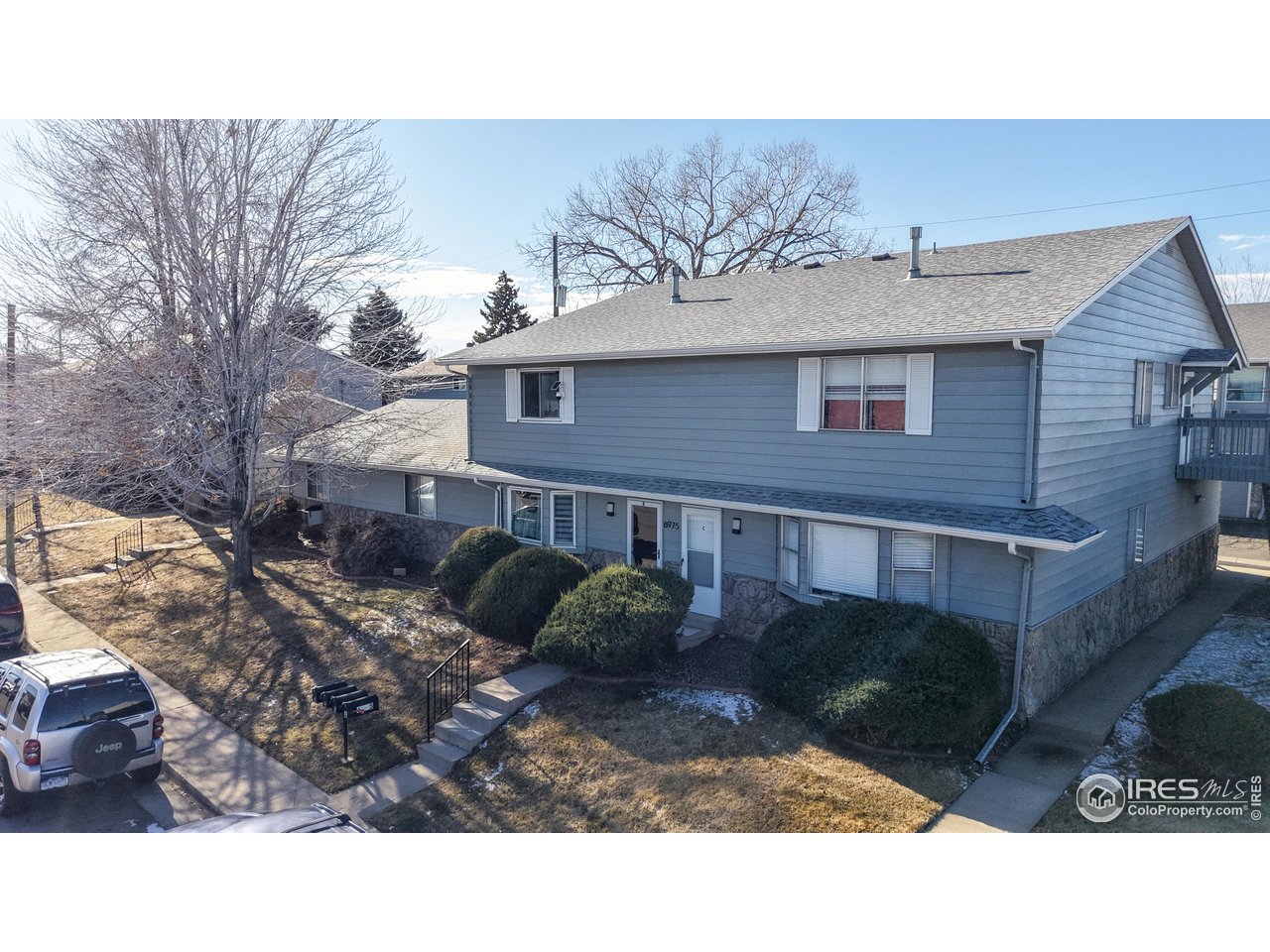 Blue two-story residential building with a stone foundation, front walkway, and leafless trees.