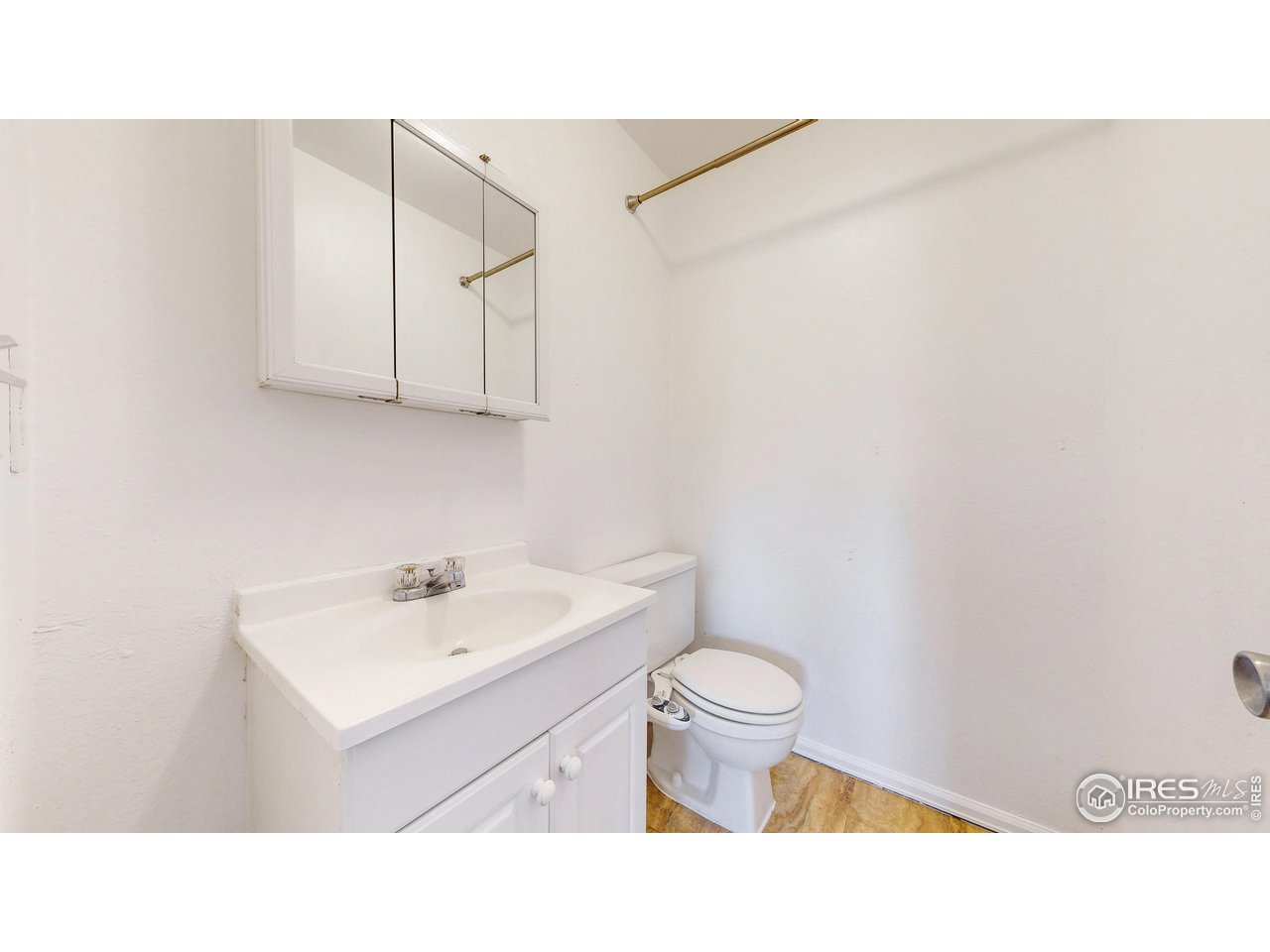 Bathroom with a white vanity, toilet, mirrored medicine cabinet, and brass towel bars.