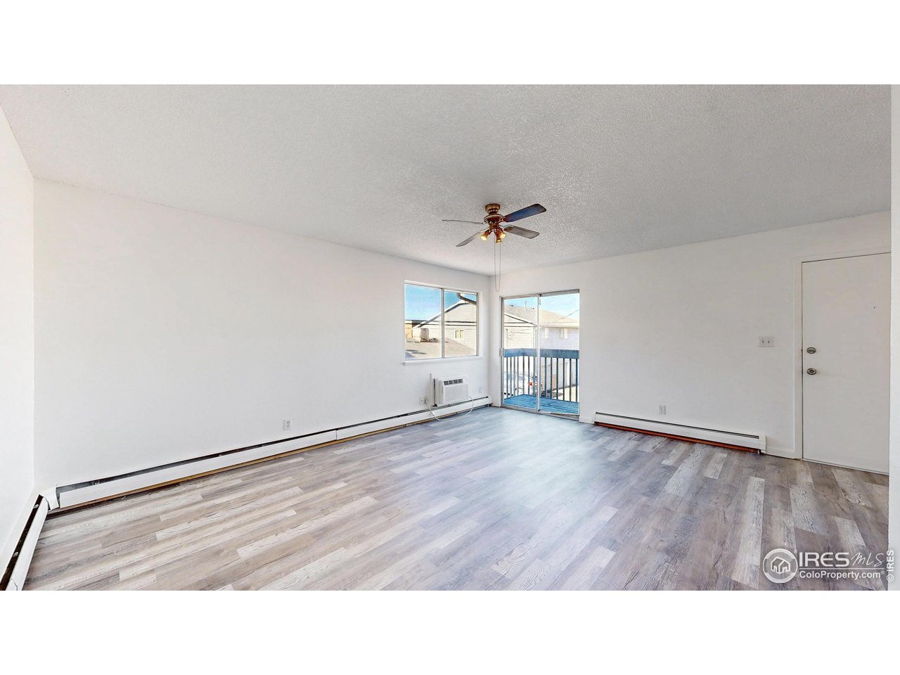 Empty living room with gray plank flooring, ceiling fan, and sliding glass door to a balcony.