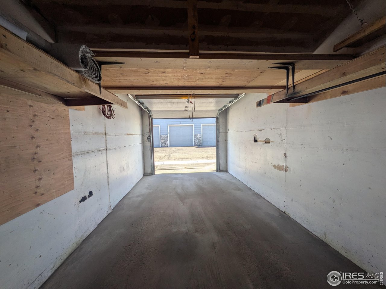 Empty garage with a concrete floor, exposed ceiling framing, and open garage door.