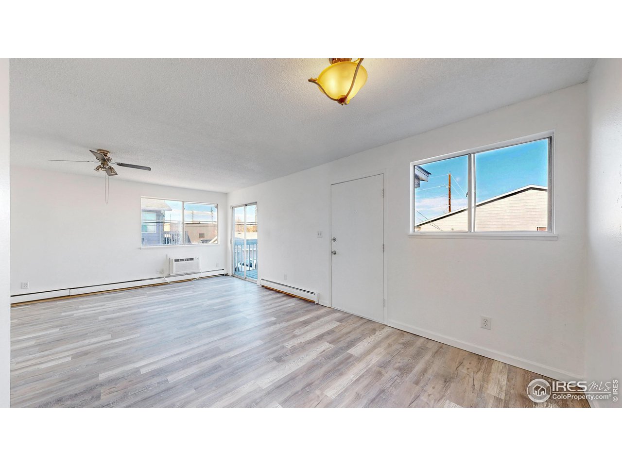 Empty living room with gray wood-look flooring, a ceiling fan, and a glass door to a small balcony.