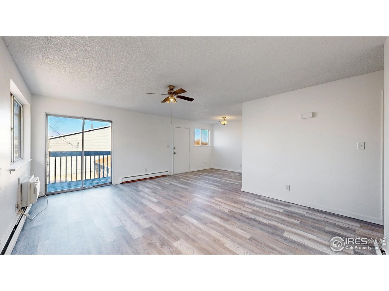 Empty living room with gray plank flooring, a ceiling fan, and a sliding glass door to a balcony.