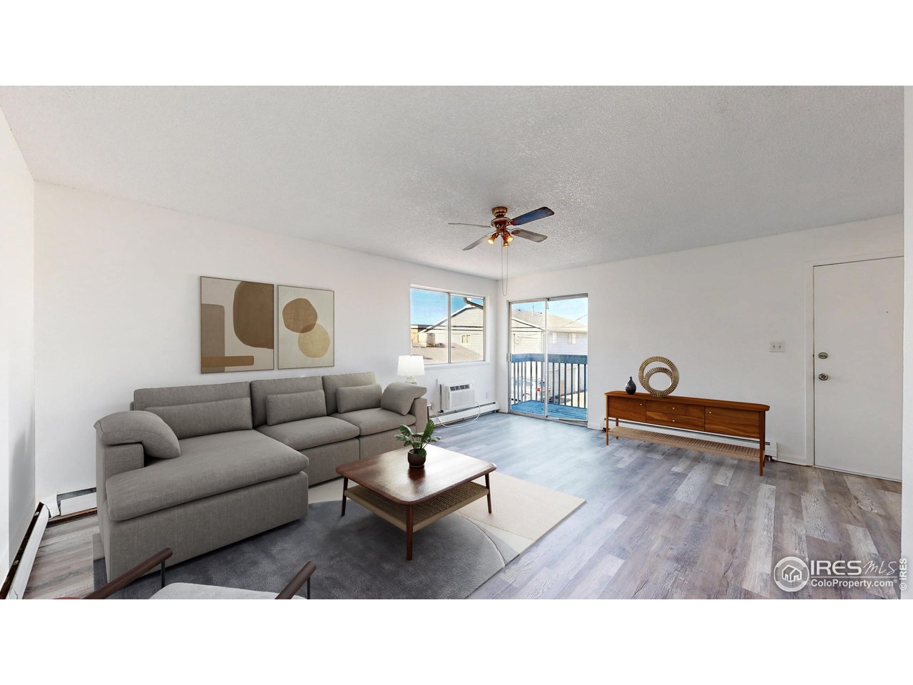 Staged living room with a gray sectional, wood furniture, and sliding glass doors to a balcony.