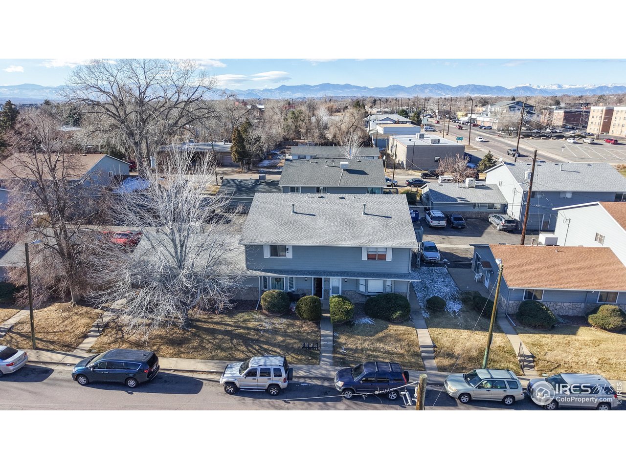 Aerial view of a blue-gray two-story home, neighboring houses, and the Rocky Mountains in the distance.