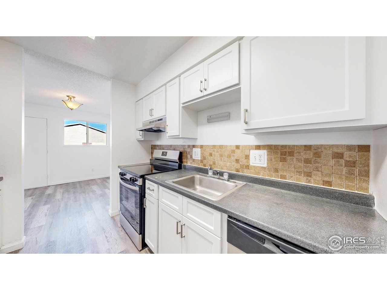 Vacant kitchen with white cabinets, tan tile backsplash, gray counters, and black appliances.