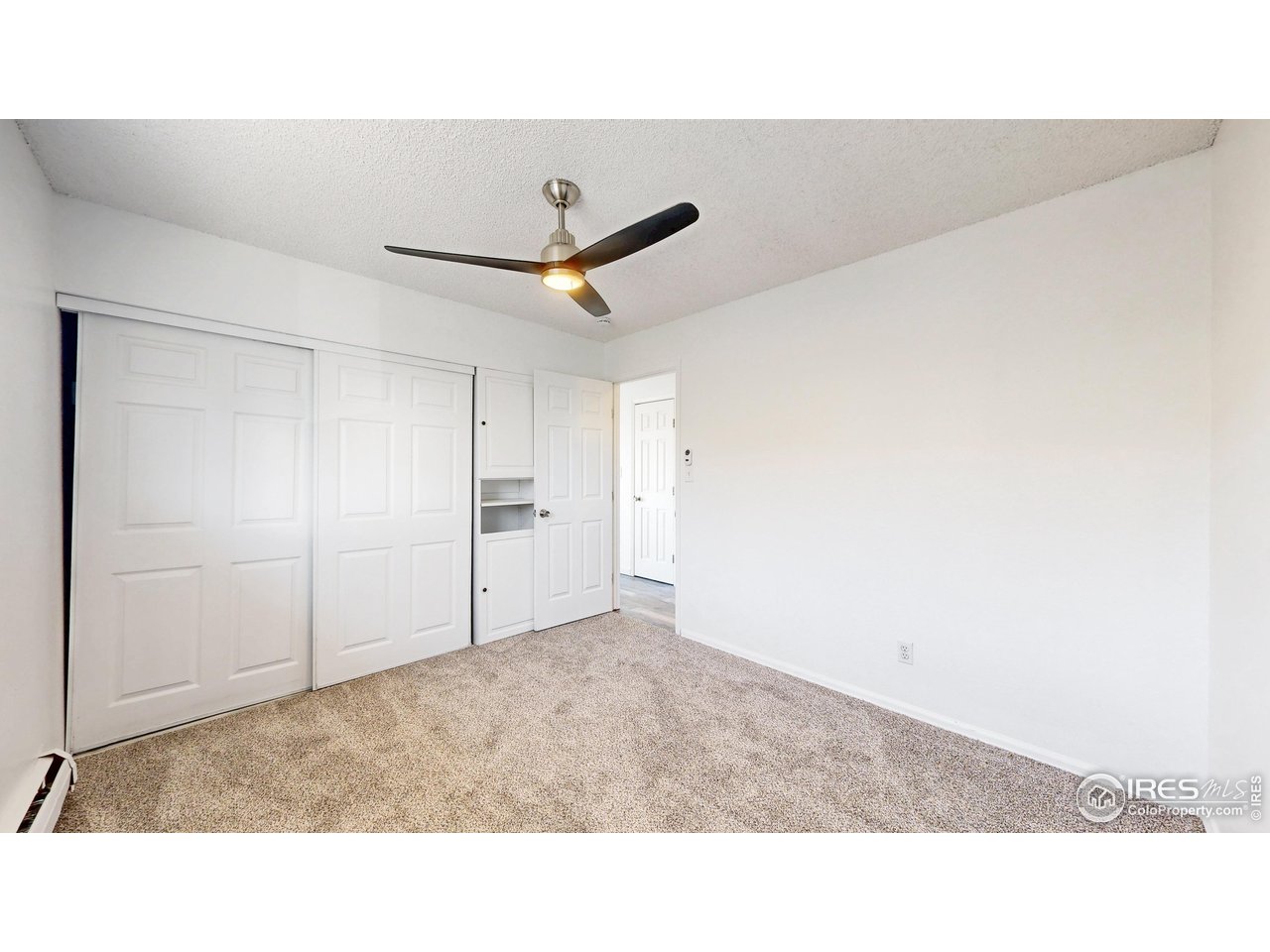 Empty carpeted bedroom with white sliding closet doors and a ceiling fan.