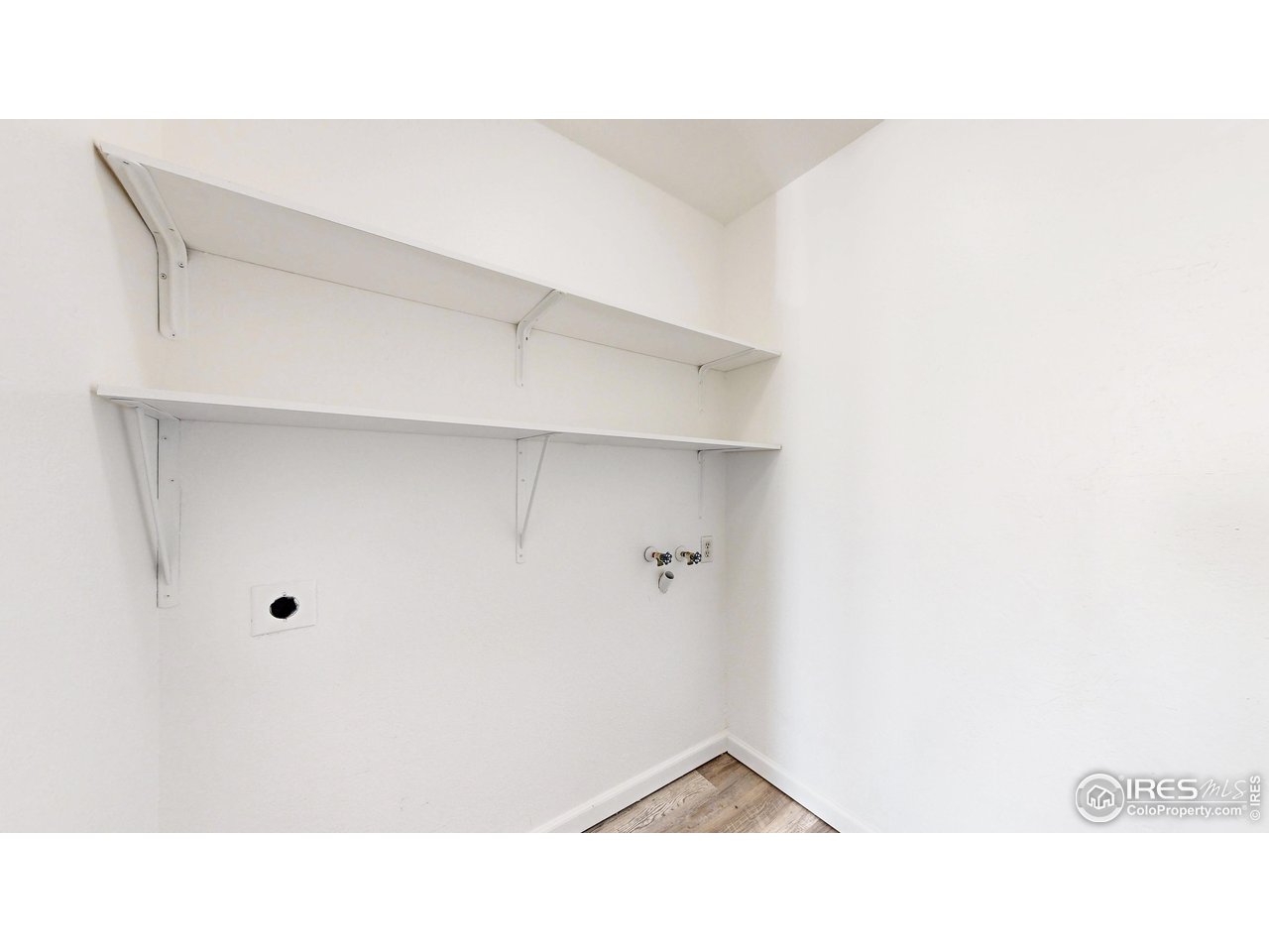 Laundry area with two white shelves, washer hookups, and wood-look flooring.