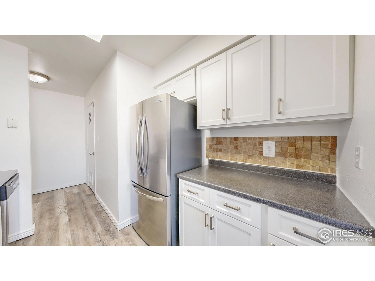 Kitchen with white cabinets, gray counters, tan tile backsplash, and a stainless steel refrigerator.
