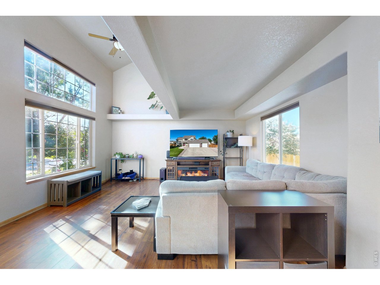 Living room with a vaulted ceiling, tall windows, hardwood floors, and a light sectional sofa.